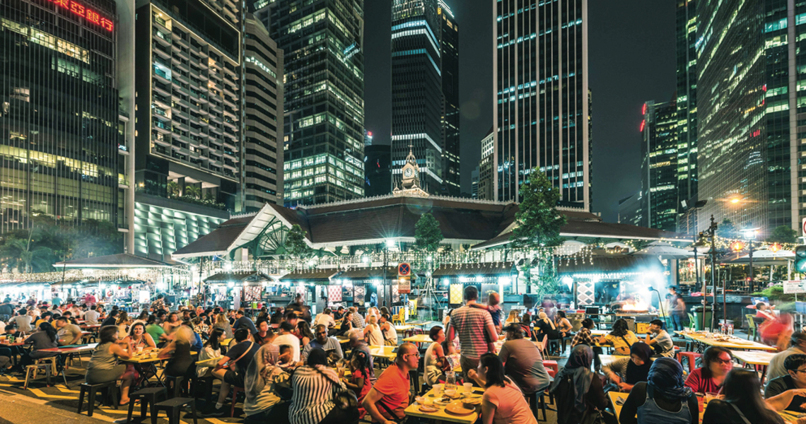 Crowded outdoor tables and smoking satay grills beneath Singapore towers at night